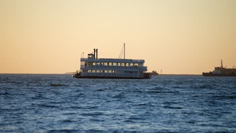 a vintage or 20th century steamboat anchored in the harbor during a golden sunset - isolated slow motion