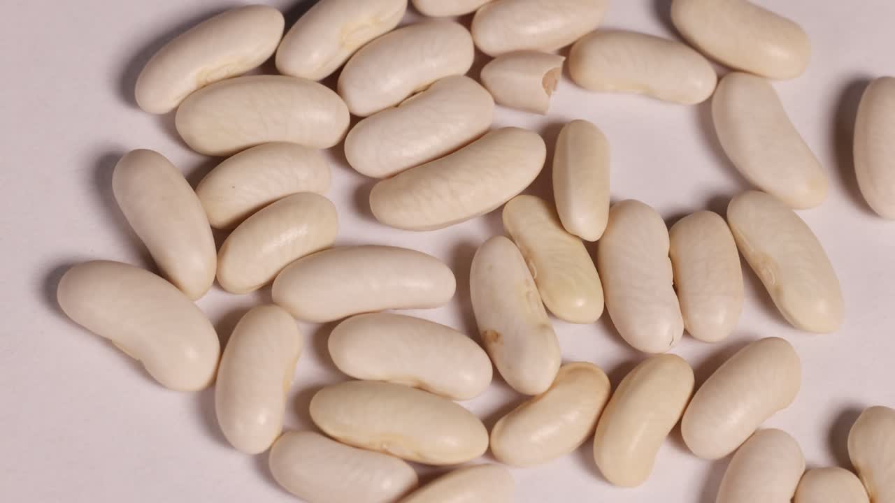 White bean seeds arranged on a dish, captured in macro detail with consistent lighting and minimal camera movement