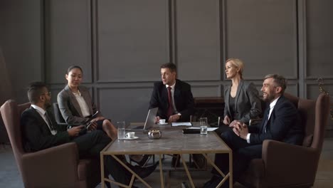 group of multiethnic corporate executives in business suits sitting around table in meeting room, passing around document on clipboard, reading and commenting on it