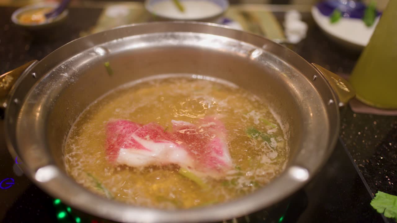 Hand dips marbled beef into simmering hotpot broth, close-up, warm lighting, shallow focus