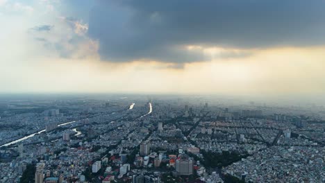 aerial view over ho chi minh city (saigon), vietnam, during sunset, as dramatic clouds cast shadows across the dense urban sprawl. a moody and cinematic atmosphere of a southeast asian metropolis.