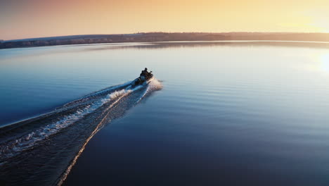boat on water surface at sunset. people driving the motor boat quickly along the evening river on beautiful water background. aerial view.