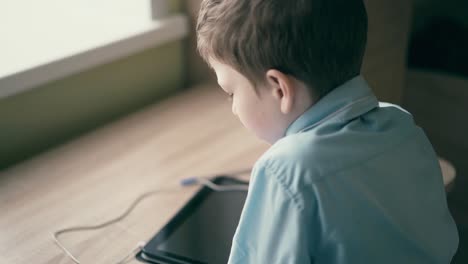 Cu-Niño-En-Cámara-Lenta-Un-Colegial-Se-Sienta-En-Una-Mesa-Y-Piensa-Que-Hay-Una-Tableta-Sobre-La-Mesa