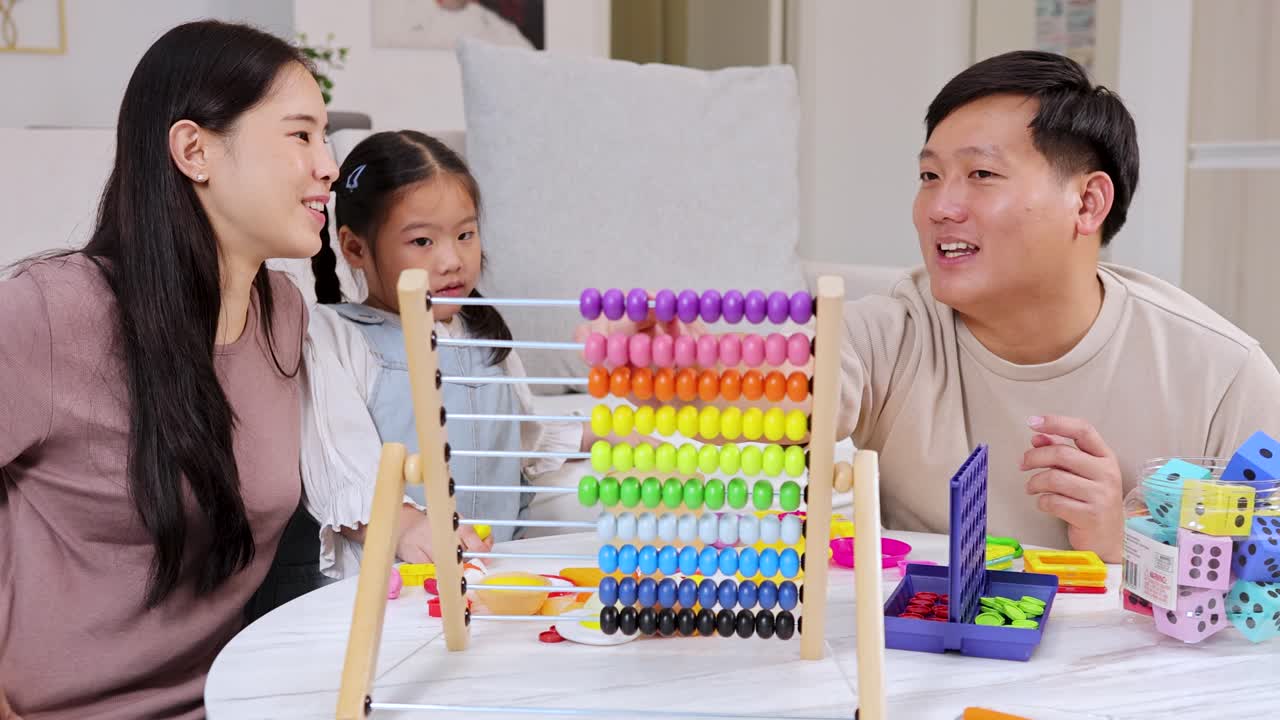 Asian parents and daughter learning with colorful abacus and toys in bright modern living room