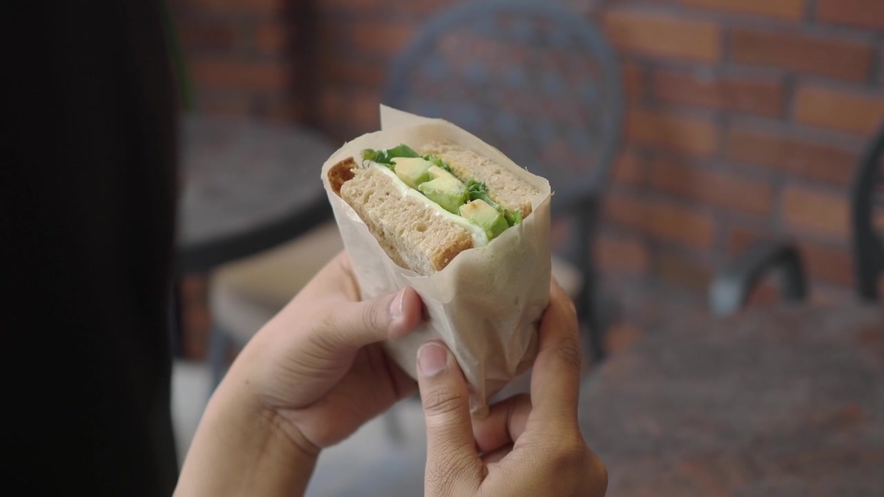 Personne tenant un sandwich frais à l'avocat dans un café