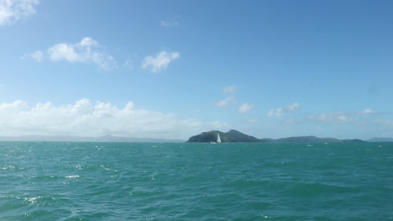 Choppy turquoise ocean, with islands and a sailboat in the distance.