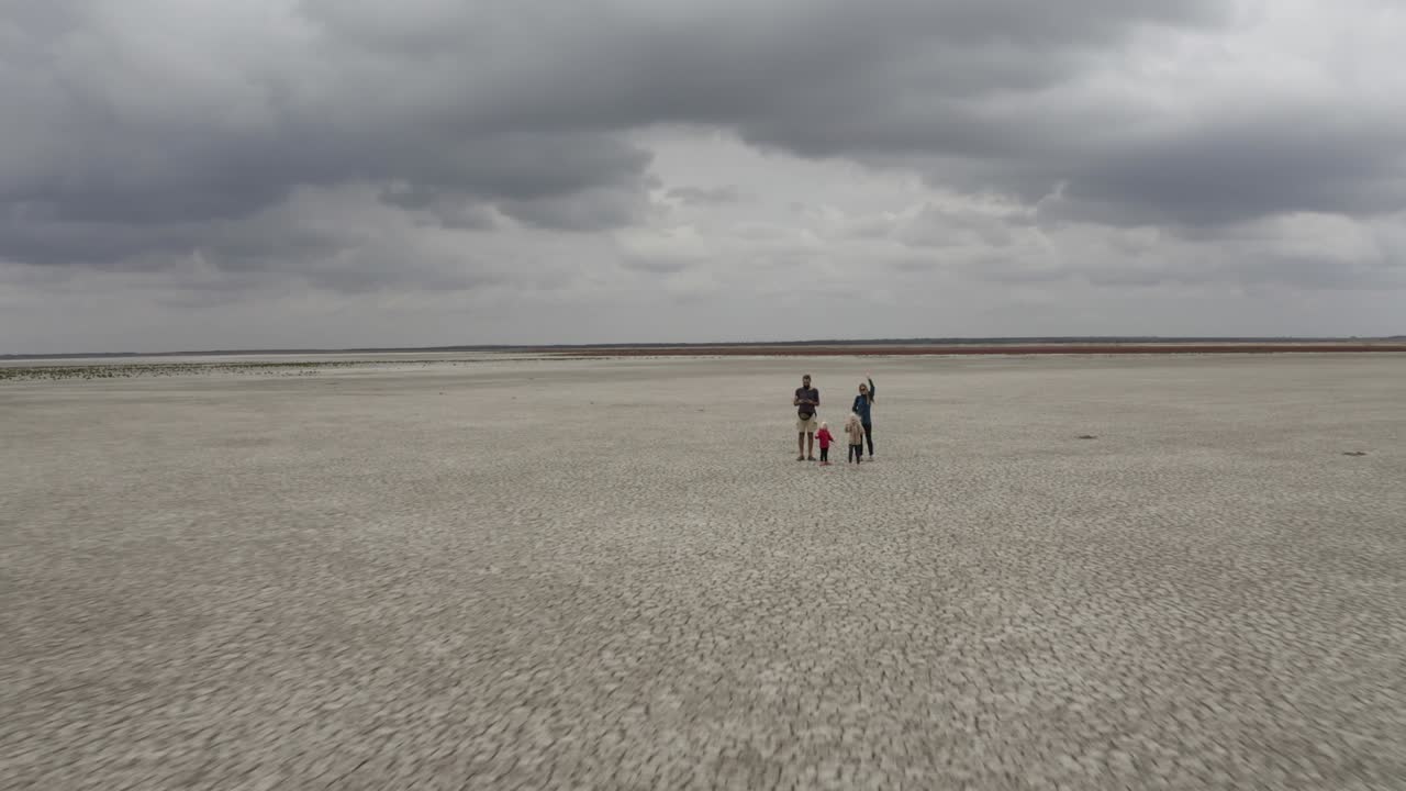 건조한 호수 한가운데 서서 카메라를 향해 손을 흔들고 있는 가족의 드론