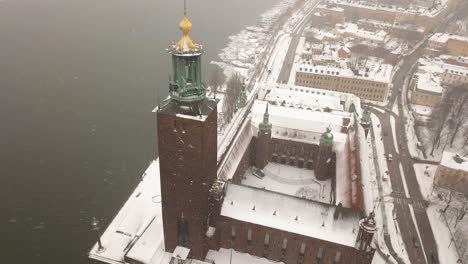 zoom out tilting aerial footage over iconic stockholm's town hall during winter storm