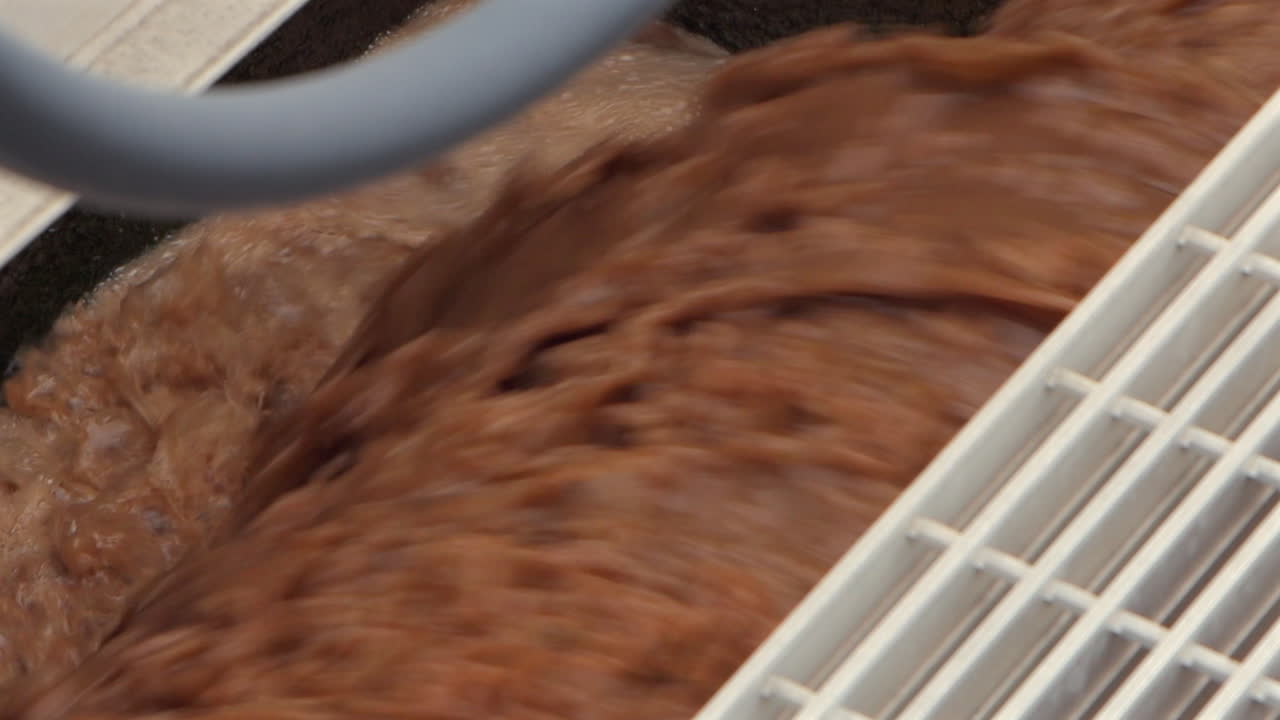 Brown sewage water churns and falls through an aeration stage at a wastewater treatment plant, showcasing the intense process of purification in motion