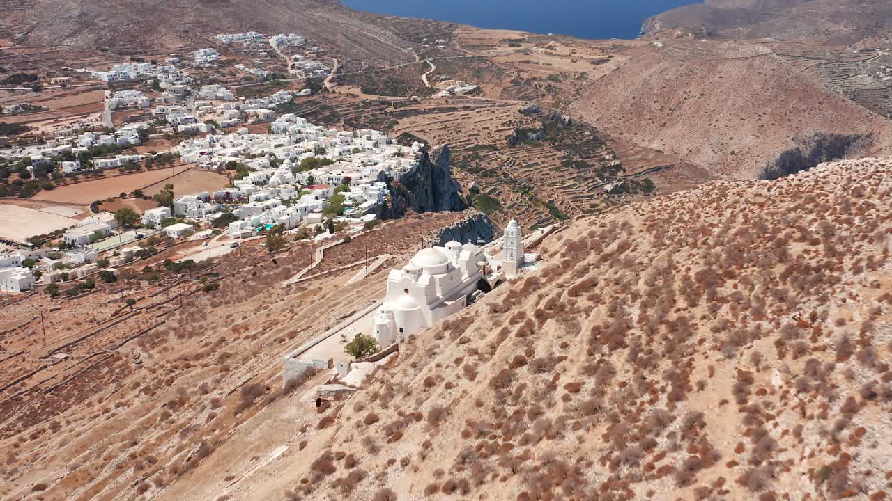 vuelo aéreo a través de la iglesia de panagia cuesta arriba y el fondo del pueblo de folegandros, grecia