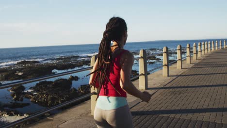 african american woman in sportswear running on promenade by the sea