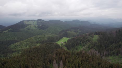 Lush-green-hills-under-overcast-skies,-vast-forest-landscape,-aerial-view