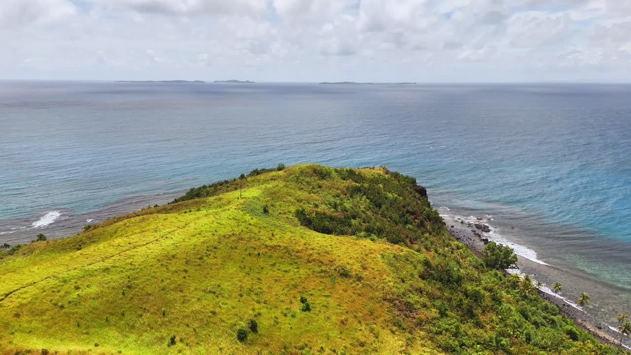 Drone image over Corregidor Island, Siargao Islands, Philippines, with lush grassy slopes, rocky shoreline, and calm blue waters of the Pacific Ocean under a bright tropical sky