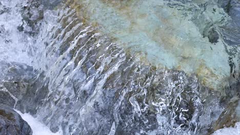 crystal-clear water cascades over moss-covered rocks in a natural mountain stream, captured in daylight with a steady, close-up camera angle