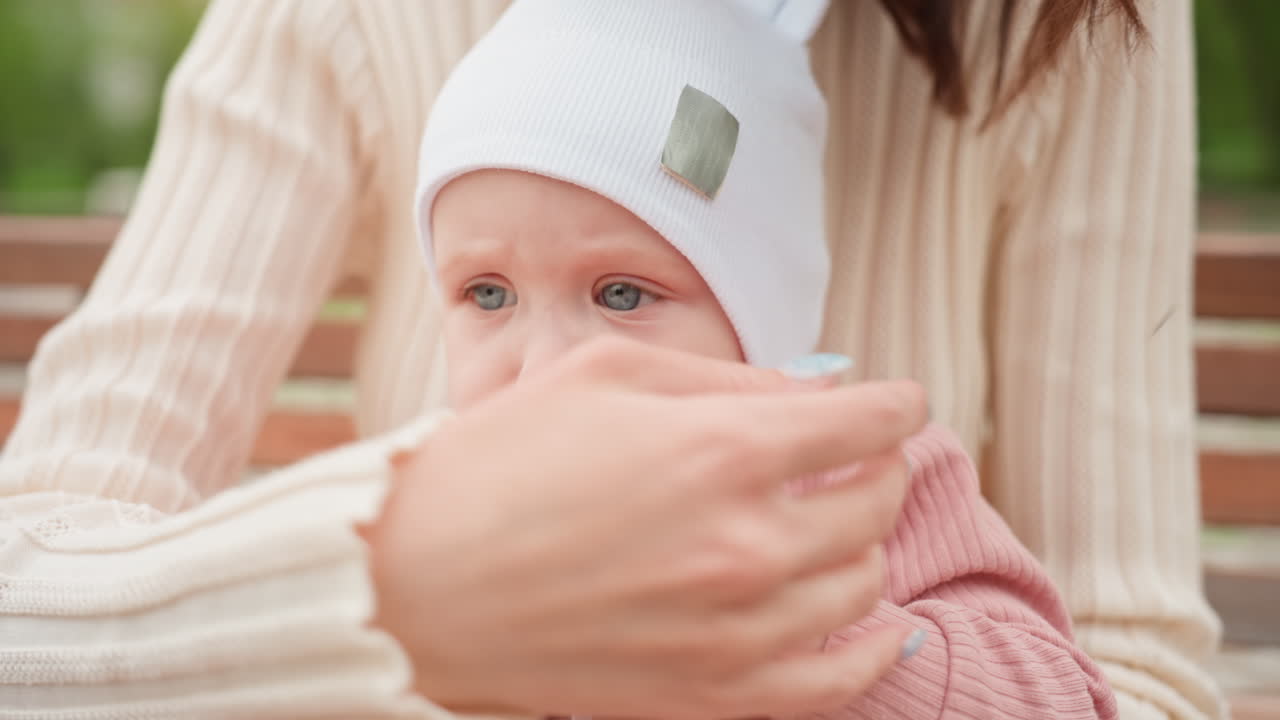 Mother Calms Infant, Caucasian Mother Gently Reassures Baby Chewing Toy On Park Bench, Mother Of Caucasian Appearance Lovingly Comforts Her Curious Baby Playing With Teether On Bench Amid Trees