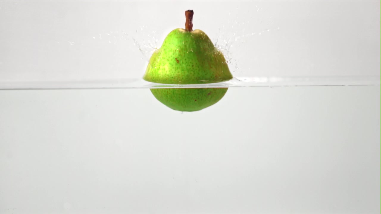 Pera verde che cade nell'acqua con uno schizzo al rallentatore