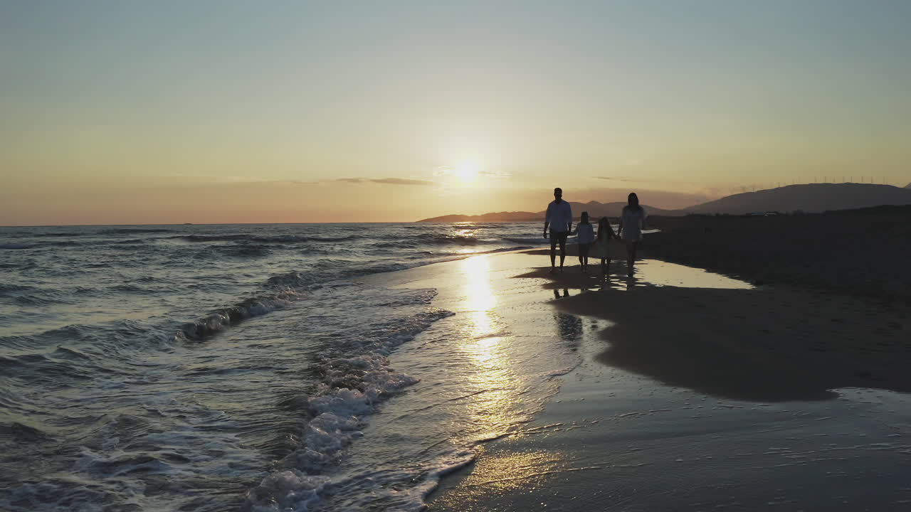 해가 지는 동안 해변에서 산책하는 가족