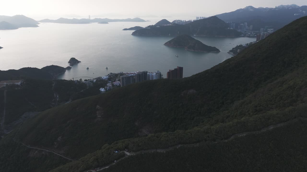 Droneoptagelse af Repulse Bay, Hong Kong. Viser gylden sandstrand, turkisblåt vand og byens skyline med omkringliggende bakker i et naturskønt kystpanorama