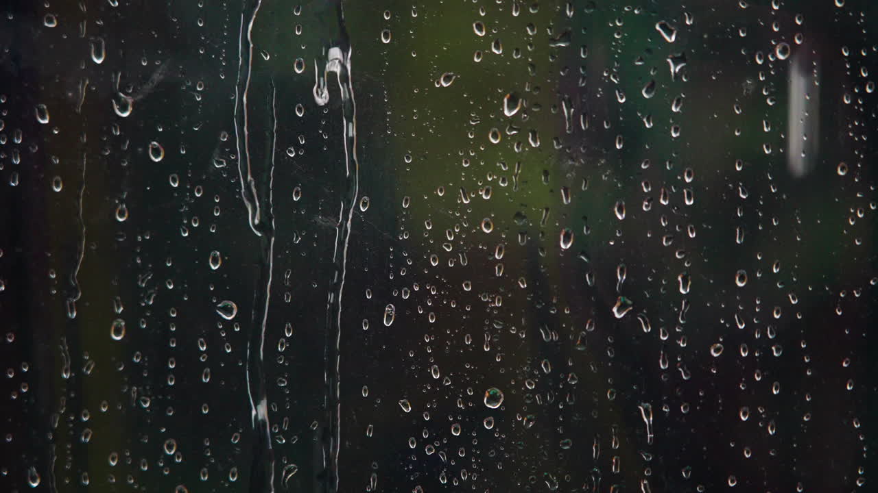 Gotas de lluvia cayendo y escurriéndose por una ventana de cristal