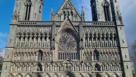 revealing shot of the front entrance of nidaros cathedral in trondheim, norway, under a clear blue spring sky, showcasing its intricate gothic architecture, detailed stone carvings and pointed arches
