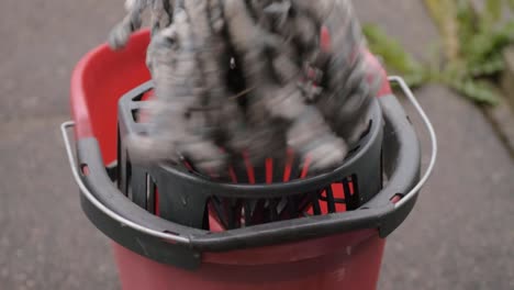 wringing cleaning mop into red bucket