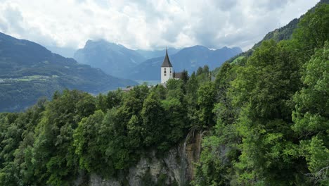 Toma-Panorámica-Aérea-De-La-Iglesia-Católica-Romana-En-Amden-Con-Fondo-Alpino-Suizo