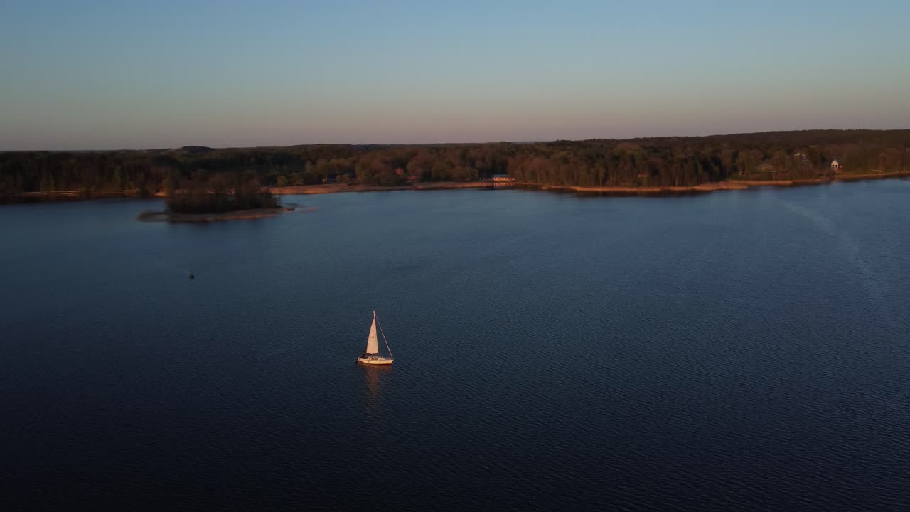 sailboat sailing on lake surrounded by forest in a spring afternoon. drone flying over view
