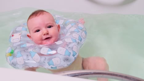 happy infant baby boy smiling while swimming in the bathtub with an inflatable ring on his neck. four month old child, close-up