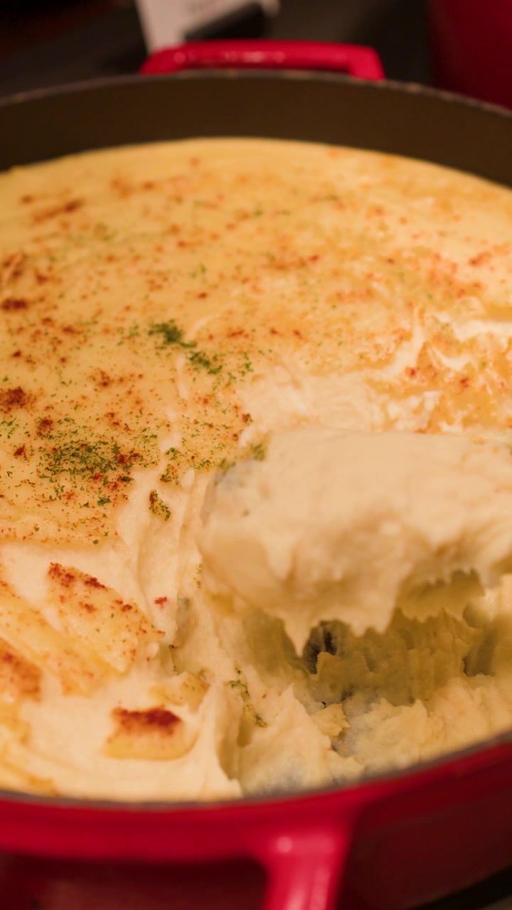 Un cucchiaio di metallo raccoglie purè di patate cremoso condito con paprika da una pentola da buffet rossa