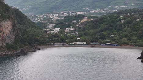 rocky bay with sand beach and mountain city in island ischia, italy, drone