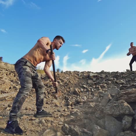 athletic men doing hard exercises with stones. shirtless sportsman breaks rocks with a sledgehammer in nature. outdoor sport. slow motion.