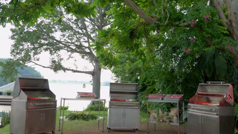 Tilt-shot-of-3-barbecue-grills-at-garden-lake-latin-mexican-party-begin-to-prepare-carne-asada-raw-meat-steak-ingredientes-onion-sausage-chorizo-salchicha-enjoy-friendship-chill-meeting