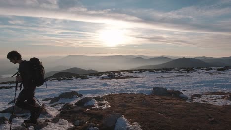 side view of young hiker with backpack and trekking poles shot against the sun in snowy guadarrama mountains, madrid, spain