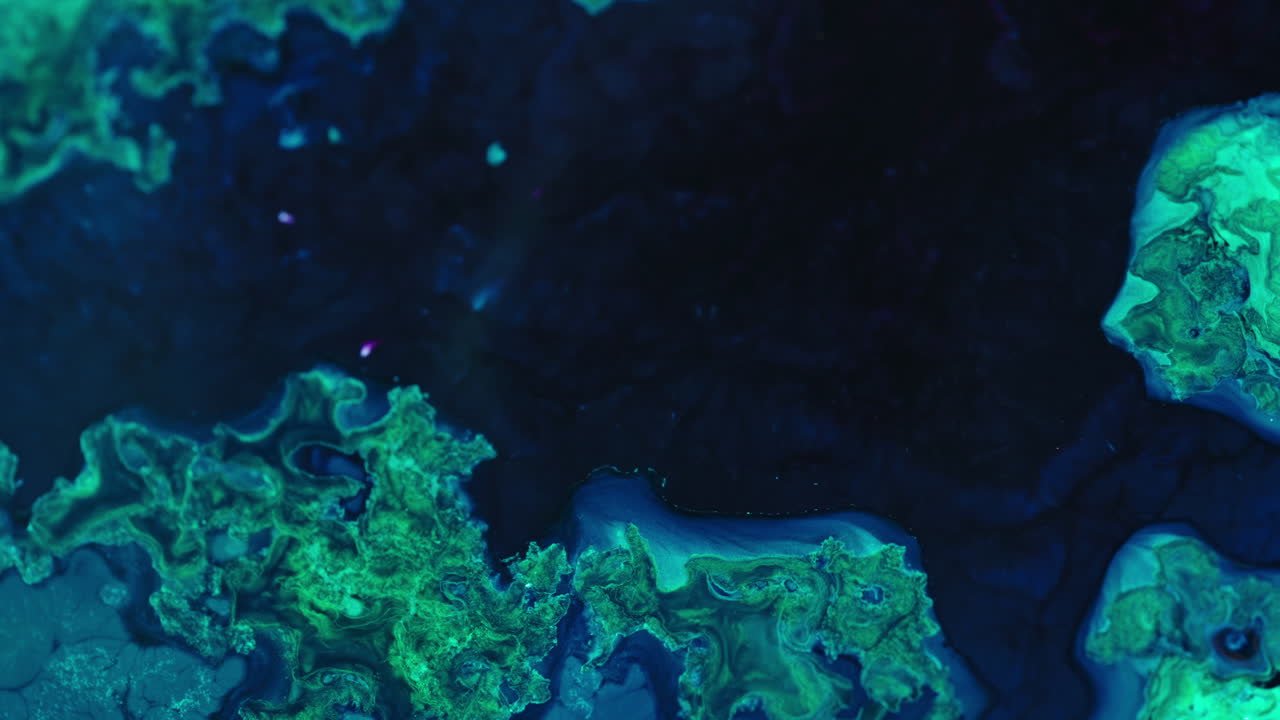 Vibrant blue and green liquids swirl and mix together in a detailed macro shot