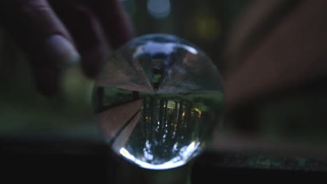 mano femenina poniendo una bola de cristal en un banco en medio de un bosque que refleja el paisaje otoñal y cambiante al revés