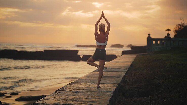 Mujer en forma en la costa de Bali durante un atardecer mágico haciendo la postura del árbol, equilibrio
