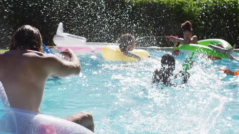 Vielfältige-Gruppe-Von-Freunden,-Die-Spaß-Daran-Haben,-Mit-Wasserpistolen-Auf-Schlauchbooten-Im-Schwimmbad-Zu-Spielen