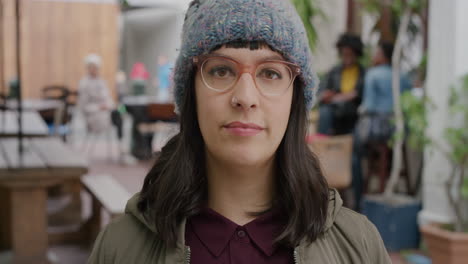 portrait of young caucasian hipster woman looking at camera serious pensive wearing beanie hat in urban outdoors restuarant background