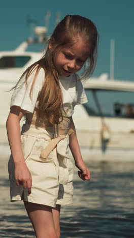 attentive brother and sister stand knee deep in sea with warm temperature water. luxurious yacht provides stunning background all bathed in warm glow of sun