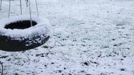 an empty tyre swing swings in the snow in winter