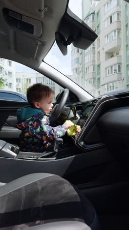 cute cheerful baby in jacket sits on driver's seat. toddler boy uses a duster cleaning car panels. vertical video.