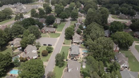 A drone zoom-in shot capturing a suburban neighborhood in the United States, showcasing tree-lined streets and residential houses. The greenery and -planned layout highlight the peaceful