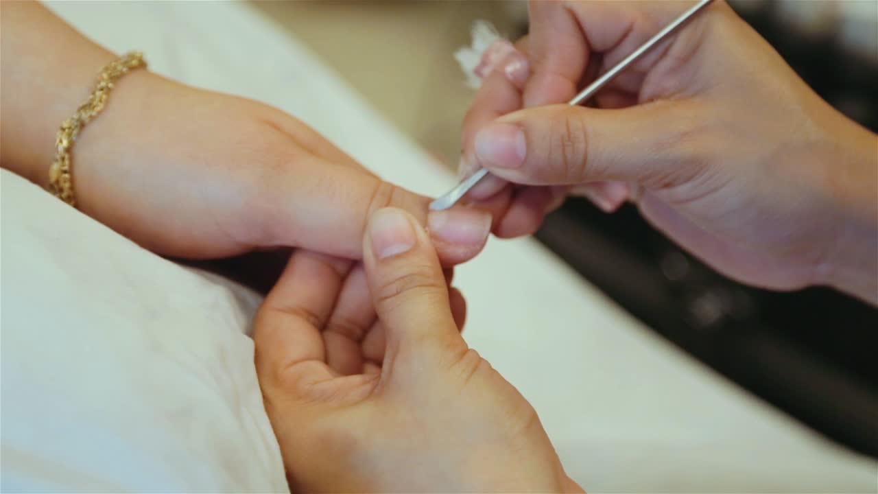 Manicurist using cuticle pusher to remove cuticles. Handheld Shot. Close up.