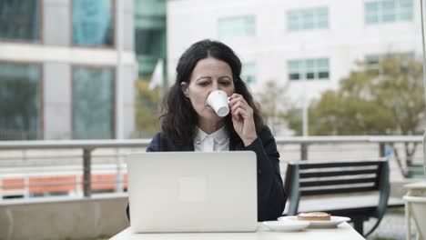 Mujer-De-Negocios-Usando-Laptop-Y-Tomando-Café-En-La-Cafetería