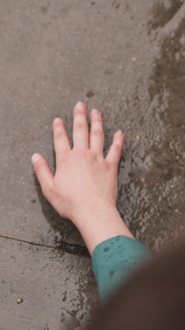 la mujer toca el suelo de hormigón húmedo en la lluvia de cerca. la mano de la dama alcanza la superficie de la piedra bajo la gota de lluvia que cae. disfrutando de la frescura en la tormenta de primavera