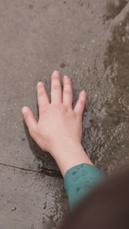 woman touches wet concrete ground at rain closeup. lady hand reaches to stone surface under falling raindrop. enjoying freshness at spring storm