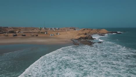 Waves-crashing-against-the-shore-with-surfers-walking-towards-the-ocean-in-Lobitos,-Peru,-South-America---Drone-Aerial-shot