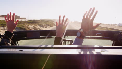 driving couple reaching hands through sunroof, back view