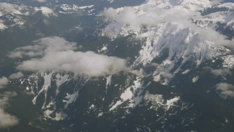 View-from-airplane-flying-over-the-Rocky-Mountains-with-low-clouds-over-mountaintops-in-Alberta-Canada-from-British-Columbia