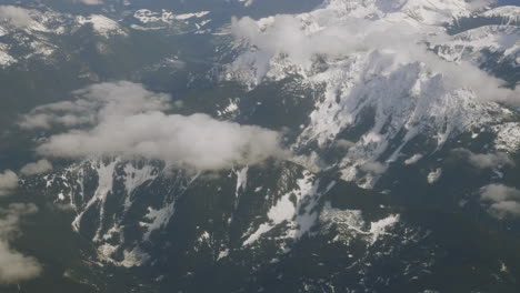 view from airplane flying over the rocky mountains with low clouds over mountaintops in alberta canada from british columbia